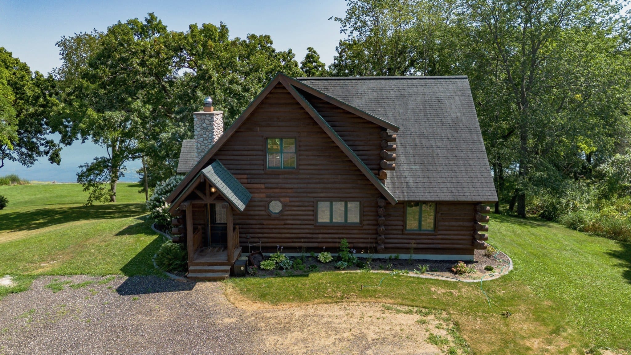 Drone view of the front of the cabin from just above the drive, with the lawn running past it to Big Twin Lake, visible through the trees on the left.